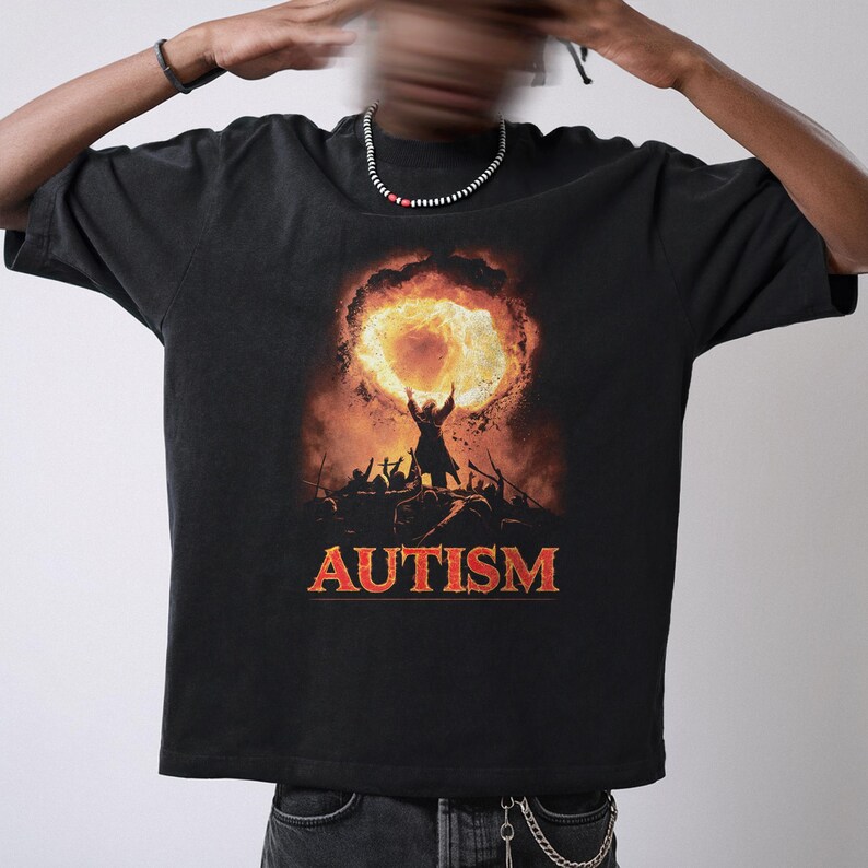 Puede incluir: Camiseta negra con un gr&aacute;fico de una persona sosteniendo un c&iacute;rculo en llamas y la palabra "AUTISM" impresa debajo.