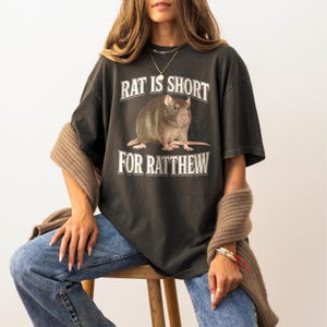 May include: A dark gray t-shirt with a graphic of a rat and the text "Rat is short for Ratthew".