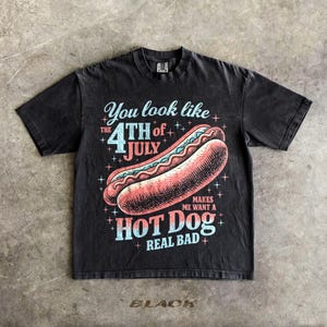 May include: Black graphic t-shirt featuring a hot dog illustration with the text "You look like the 4th of July makes me want a hot dog real bad." The shirt has a vintage, distressed look.
