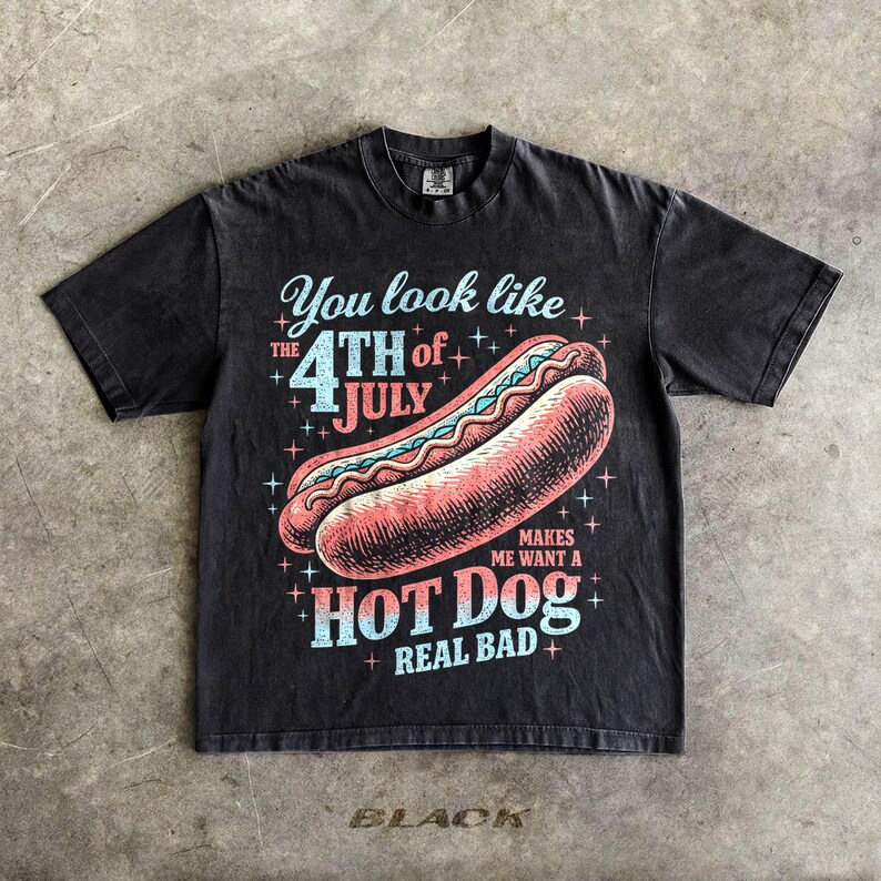 May include: Black graphic t-shirt featuring a hot dog illustration with the text "You look like the 4th of July makes me want a hot dog real bad." The shirt has a vintage, distressed look.