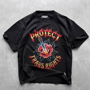 Peut inclure: T-shirt noir avec un imprimé graphique d'une rose et d'une dague avec le texte "Protect Trans Rights" en flammes.