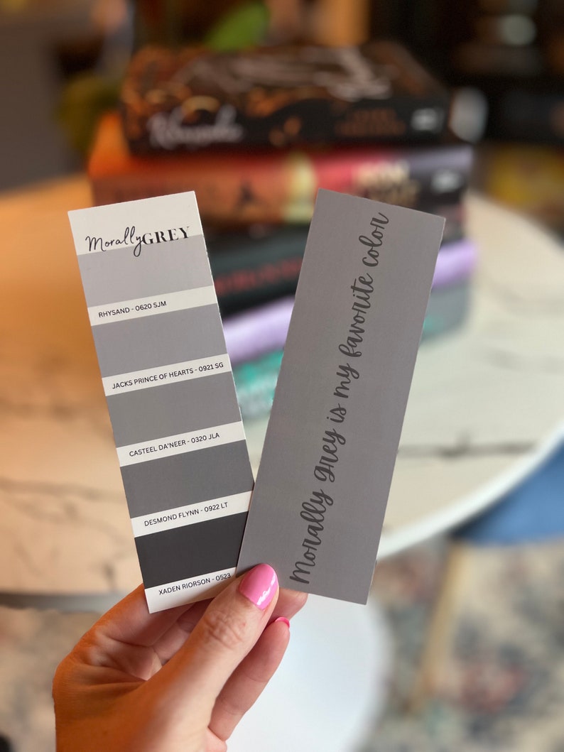 May include: A gray paint color chart with the text "MorallyGREY" at the top. The chart shows five different shades of gray with corresponding names and numbers. A separate gray card with the text "Morally grey is my favorite color" is held in a hand.