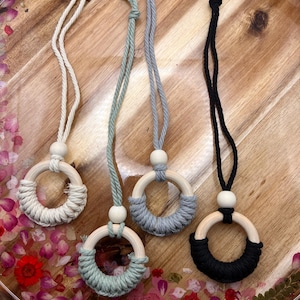 May include: Four macrame car air fresheners in a variety of colors: cream, light green, gray, and black. Each has a wooden ring wrapped with yarn and a wooden bead. They hang from a matching cord.