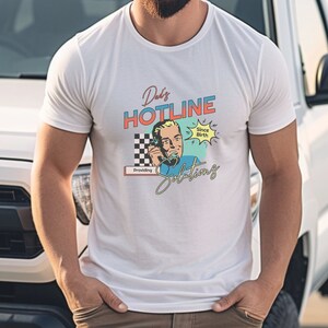 May include: White t-shirt with a retro-style graphic design featuring a man on the phone. The graphic says "Dad's Hotline Providing Solutions Since Birth".