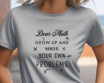 May include: A grey t-shirt with a black graphic that says "Dear Math, Grow Up and Solve Your Own Problems". The graphic includes mathematical symbols such as greater than, less than, multiply, divide, and square root.