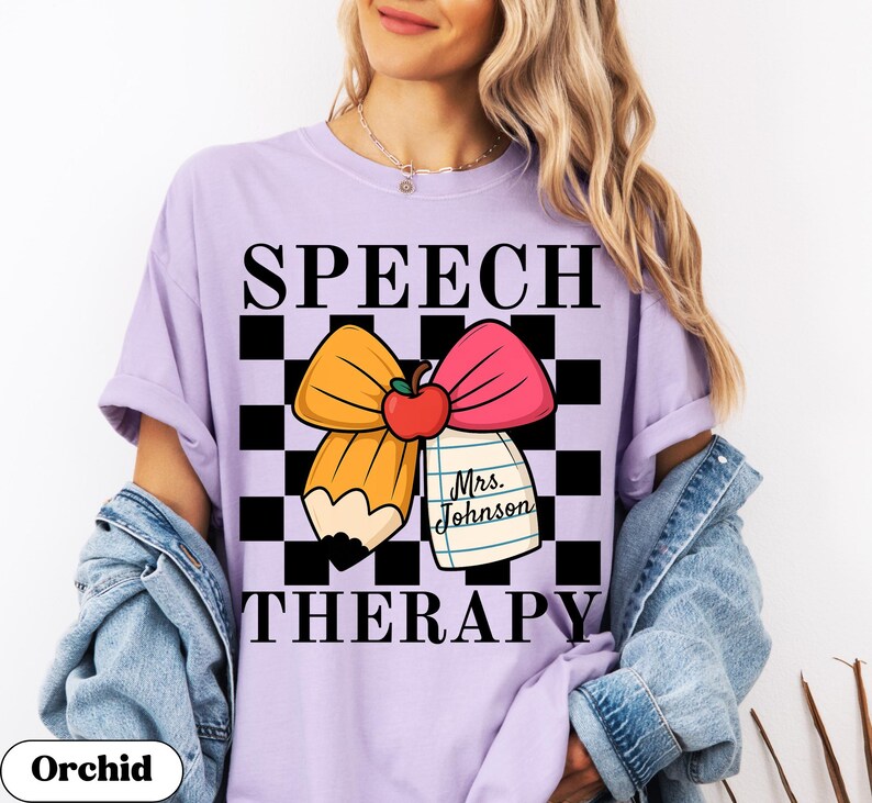 May include: Orchid purple t-shirt with a graphic design for speech therapy. The design features a pencil, bow, apple, and the text "SPEECH THERAPY" in black. A notepad with the name "Mrs. Johnson" is also included.