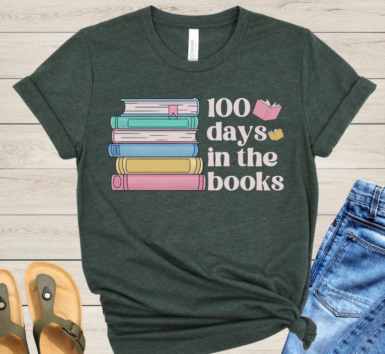 Pu&ograve; includere: Una maglietta verde scuro con una pila di libri colorati e il testo "100 giorni tra i libri".