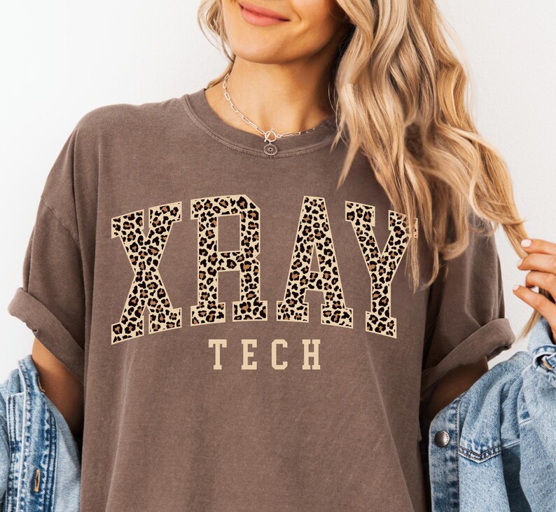 May include: A brown t-shirt with the words "XRAY TECH" printed in white letters. The word "XRAY" is in a leopard print font.