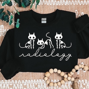 May include: Black sweatshirt with a white graphic of three skeleton cats and the text "radiology".