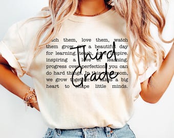 May include: Cream-colored t-shirt with the words "Third Grade" in a bold font. The shirt features a quote about teaching and inspiring a love of learning. The text is in black.