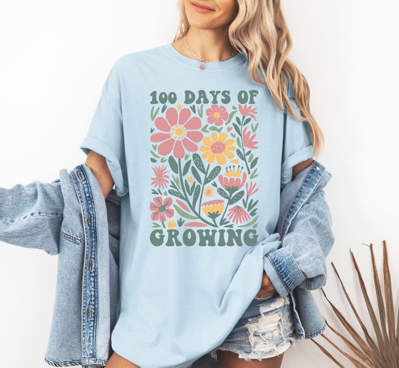 May include: A light blue t-shirt with a graphic of colorful flowers and the text "100 Days of Growing" in a retro font.