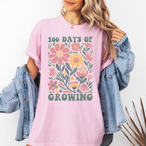 May include: Pink t-shirt with a floral design and the text "100 Days of Growing" in a retro font.