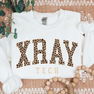 May include: White sweatshirt with a leopard print graphic that says "XRAY TECH" in a collegiate font.
