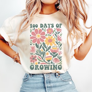 May include: A white t-shirt with a floral design and the text "100 Days of Growing". The flowers are pink, yellow, and green.