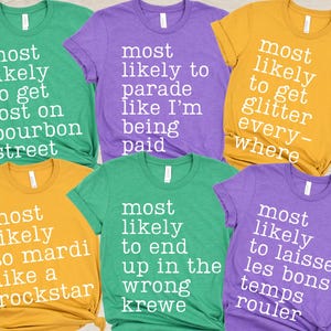 May include: Several brightly coloured t-shirts, including green, purple, and gold, each with a different white text slogan. Phrases include "Most Likely to Get Lost on Bourbon Street" and "Most Likely to Parade like I'm being paid."