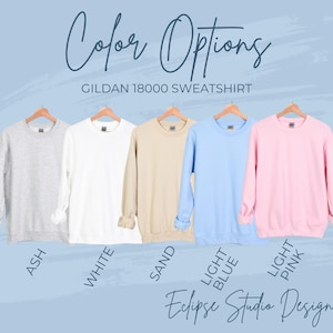 May include: A display of Gildan 18000 sweatshirts in various colors: ash, white, sand, light blue, and light pink. The text "Color Options" and "Eclipse Studio Design" are also visible.