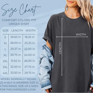 May include: Size chart for a unisex t-shirt in Comfort Colors 1717. The chart shows the length and width measurements in inches for sizes S, M, L, XL, 2XL, 3XL, and 4XL. The model is wearing a size XL t-shirt, which is two sizes larger than their usual size M. The text reads "Model normally wears size M but is wearing size XL in this image. Size up 2 sizes for this oversized look."