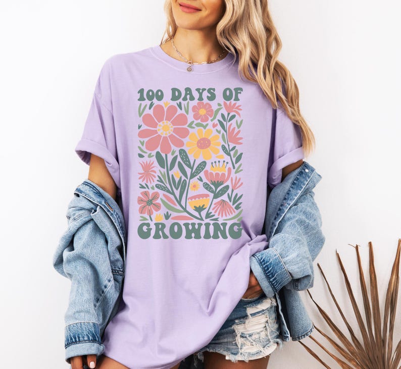 May include: A lavender t-shirt with a graphic design of colorful flowers and the text "100 Days of Growing" in a retro font.