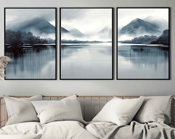 May include: Three framed abstract landscape paintings in a blue and grey colour scheme. The paintings depict a misty lake with mountains in the background. The paintings are hung on a white wall above a sofa with cushions and a throw.