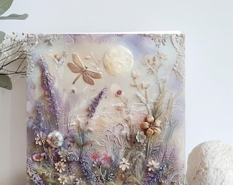 May include: A square mixed-media wall art piece featuring a textured, raised relief of a dragonfly in flight, a full moon, and various wildflowers in shades of lavender, cream, and soft gold against a pale, ethereal, painted background.