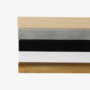 May include: A stack of five rectangular wooden frames in various colors. The colors include natural wood, gray, black, white, and gold. The frames are stacked horizontally, showcasing their different finishes.