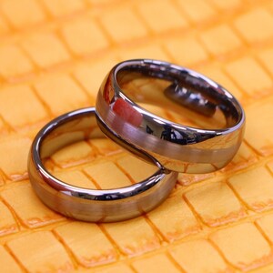 May include: Two silver wedding bands on a yellow textured surface.