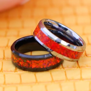 May include: Two tungsten carbide rings with a red opal inlay. One ring is black and the other is silver.
