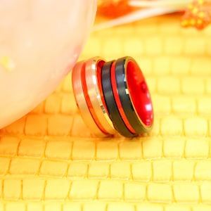 May include: Three stacked rings, one with a black and red band, one with a black band, and one with a silver band.