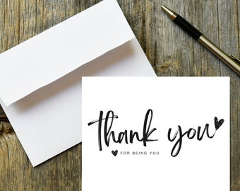May include: A white card with black calligraphy that reads "thank you" with a small heart symbol. Below the text is "for being you" with a small heart symbol.