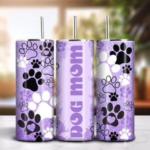 May include: Three stainless steel tumblers with lids and straws. The tumblers are decorated with a purple glitter background and black and white paw prints. One tumbler has the text "Dog Mom" in purple.