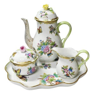 May include: A white porcelain tea set featuring a teapot, a lidded sugar bowl, a creamer, and a scalloped tray. Each piece is decorated with colorful floral patterns and butterflies, accented with gold trim and sculpted flower finials.