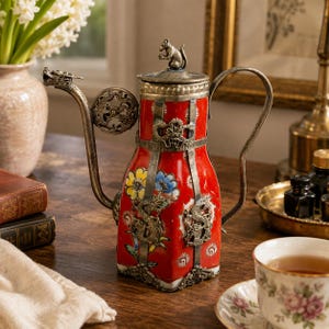 Könnte beinhalten: Eine rote Keramikteekanne mit einem silberfarbenen Metallrahmen mit Drachenmotiven, einem drachenförmigen Ausguss und einem Deckel, der mit einer kleinen Rattenfigur verziert ist. Der Körper ist mit bunten Blumenmustern und silbernen Drachenakzenten versehen.