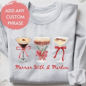May include: Gray sweatshirt with a Christmas-themed design featuring three cocktails with red bows and the text "Merrier With A Martini".