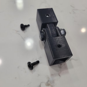 May include: A black 3D printed hinge with two black screws.