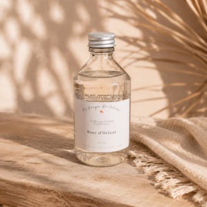 Peut inclure: Une bouteille en verre transparent remplie de liquide, dotée d'un bouchon à vis argenté et d'une étiquette blanche. L'étiquette porte le texte Ma Bougie Bordelaise, Recharge parfum d'ambiance, Rose d'Orient et 250 ml. Corps cylindrique.