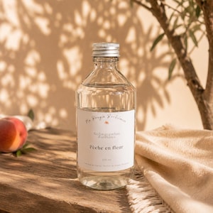 Peut inclure: Une bouteille en verre transparent avec un bouchon à vis argenté contenant 250 ml de liquide. L'étiquette blanche porte le texte Ma Bougie Bordelaise, Recharge parfum d'ambiance, Pêche en fleur et 250 ml, avec un petit motif pêche.