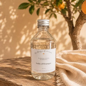 Peut inclure: Une bouteille en verre transparent avec un bouchon à vis argenté contenant 250 ml de liquide. L'étiquette blanche porte le texte Ma Bougie Bordelaise, Recharge parfum d'ambiance, Voile d'Oranger, 250 ml, Fabriqué en France - Parfum de Grasse - Artisan.