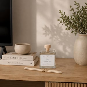 Peut inclure: Un flacon diffuseur à roseaux en verre carré avec un bouchon en bois clair et une étiquette blanche portant l'inscription Brume de Soleil, accompagné d'un faisceau de fins roseaux en bois liés par une ficelle, posé sur une surface en bois.