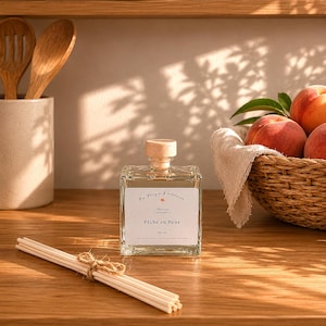 Peut inclure: Un flacon diffuseur de parfum carré en verre avec un bouchon en bois clair et une étiquette blanche portant l'inscription Ma Bougie Bordelaise Pêche en fleur 100 ml. Un faisceau de bâtonnets blancs liés par une ficelle est posé devant.