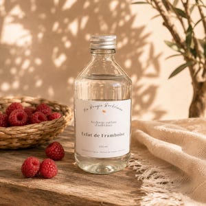 Peut inclure: Une bouteille en verre transparent avec un bouchon à vis argenté contenant un liquide, dotée d'une étiquette blanche avec le texte Ma Bougie Bordelaise, Recharge parfum d'ambiance, Eclat de Framboise et 250 ml, placée près de framboises fraîches.