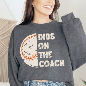 Könnte beinhalten: Ein dunkel-heathergraues Sweatshirt mit einer Vintage-Baseballgrafik und dem Text "Dibs on the Coach".