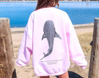 May include: A light pink sweatshirt with a whale shark graphic on the back. The text "When you go through deep waters, I will be with you. Isaiah 43:2" is printed below the graphic.