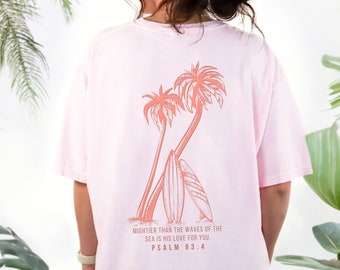 May include: Pink t-shirt with a graphic of palm trees and surfboards. The text "MIGHTER THAN THE WAVES OF THE SEA IS HIS LOVE FOR YOU. PSALM 93:4" is printed on the back of the shirt.