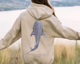 May include: A beige hoodie with a whale shark graphic on the back. The hoodie has a quote from Isaiah 43:2, "When you go through deep waters, I will be with you."