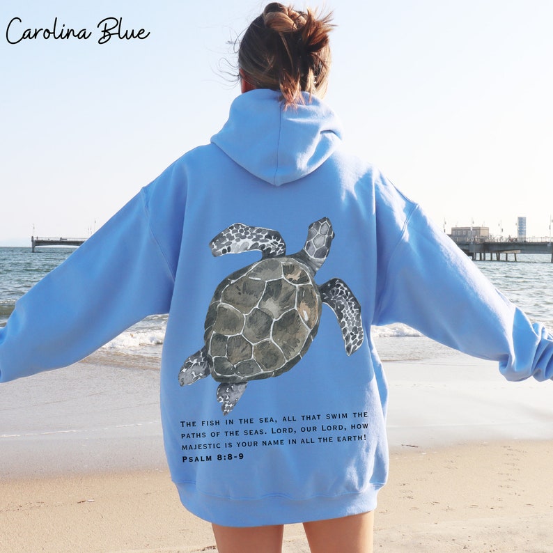 May include: A light blue hooded sweatshirt with a watercolor illustration of a sea turtle on the back. The text "THE FISH IN THE SEA, ALL THAT SWIM THE PATHS OF THE SEAS. LORD, OUR LORD, HOW MAJESTIC IS YOUR NAME IN ALL THE EARTH! PSALM 8:8-9" is printed below the turtle.