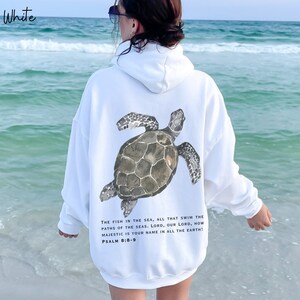 May include: White hooded sweatshirt with a sea turtle graphic and the text "THE FISH IN THE SEA, ALL THAT SWIM THE PATHS OF THE SEAS. LORD, OUR LORD, HOW MAJESTIC IS YOUR NAME IN ALL THE EARTH! PSALM 8:8-9"