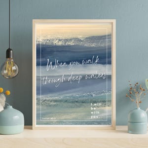 May include: A framed print with a blue and white watercolor background depicting waves. The text "When you walk through deep waters" is written in white cursive script. The text "Isaiah 43:2" is written in smaller white text below the waves. The text "I will be with you." is written in white cursive script below the waves.