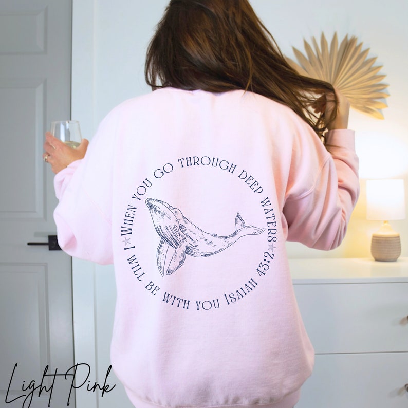 May include: A light pink sweatshirt with a blue whale graphic and the text "When you go through deep waters I will be with you Isaiah 43:2".