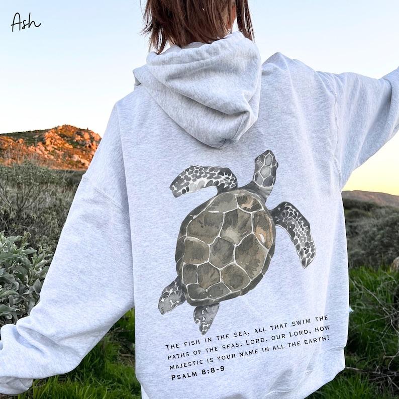 May include: Gray hooded sweatshirt with a watercolor illustration of a sea turtle on the back. The text "THE FISH IN THE SEA, ALL THAT SWIM THE PATHS OF THE SEAS. LORD, OUR LORD, HOW MAJESTIC IS YOUR NAME IN ALL THE EARTH! PSALM 8:8-9" is printed below the turtle.