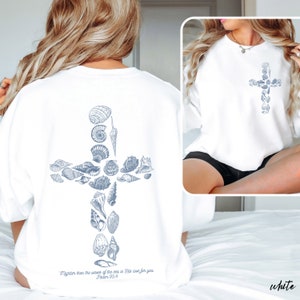 May include: White sweatshirt featuring a cross design made of seashells. The back of the sweatshirt has a larger cross design, while the front has a smaller version. The text "Mightier than the waves of the sea is His love for you Psalm 93.4" is printed on the back.